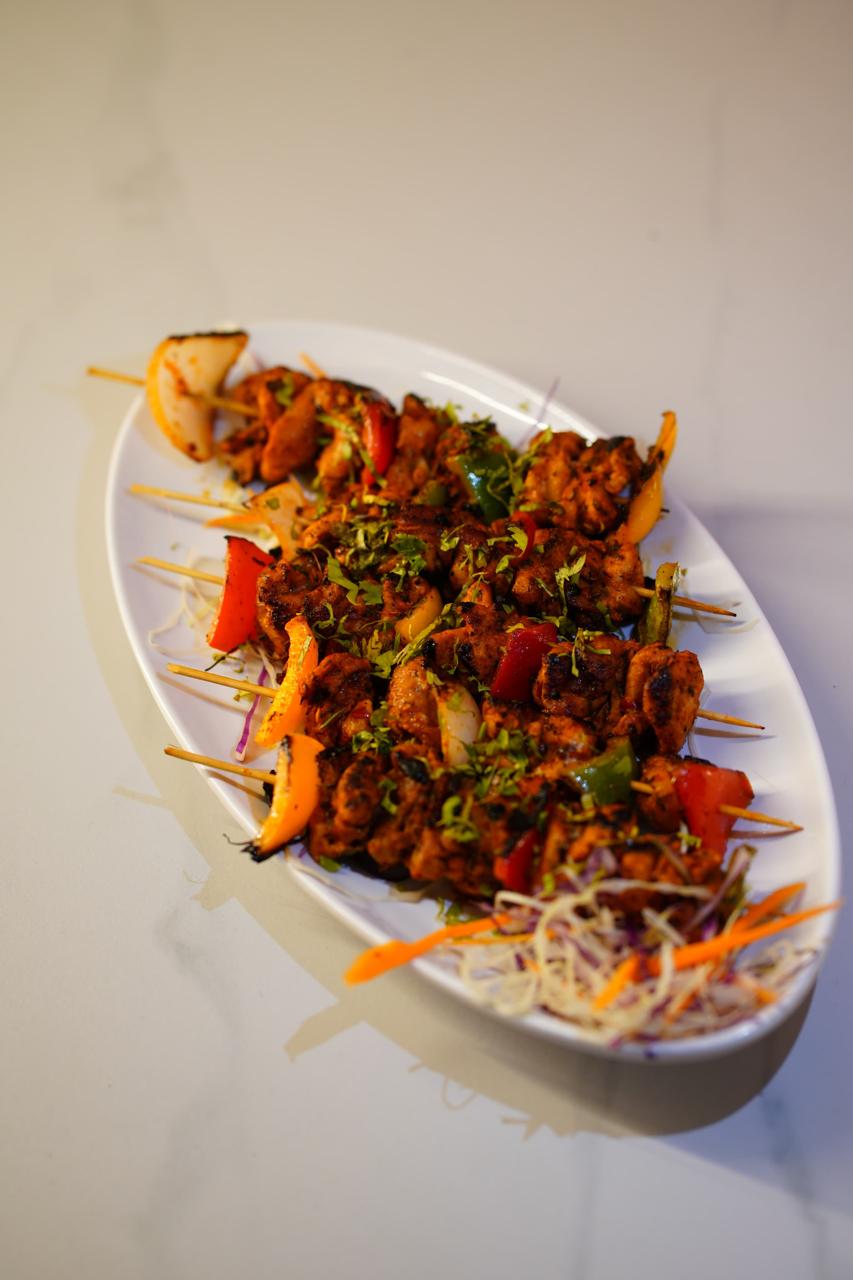 Chilli lemon chicken skewers on a white oval plate — charred chicken with peppers and onion on wooden sticks, scattered with coriander, on shredded cabbage and carrot